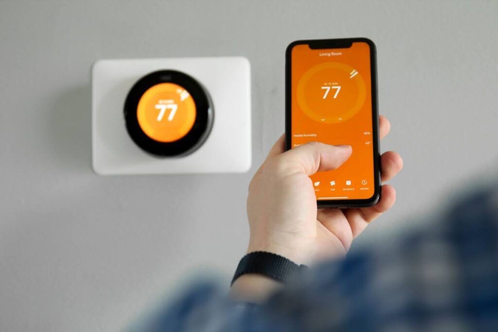 man holding his cellphone to control the smart thermostat on the wall